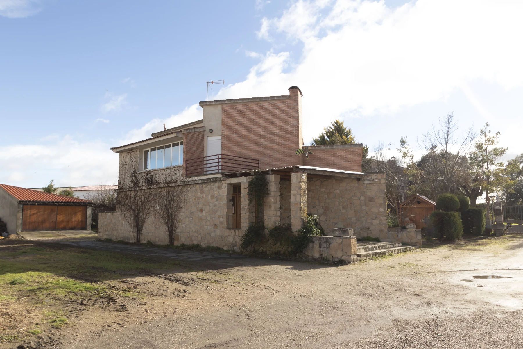 Fotografía del estado existente de una vivienda con fábrica de ladrillo y piedra, porche y jardín