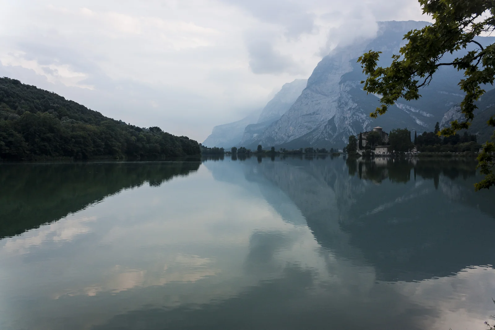 Un castillo junto a un lago de montaña con nubes reflejadas en el agua
